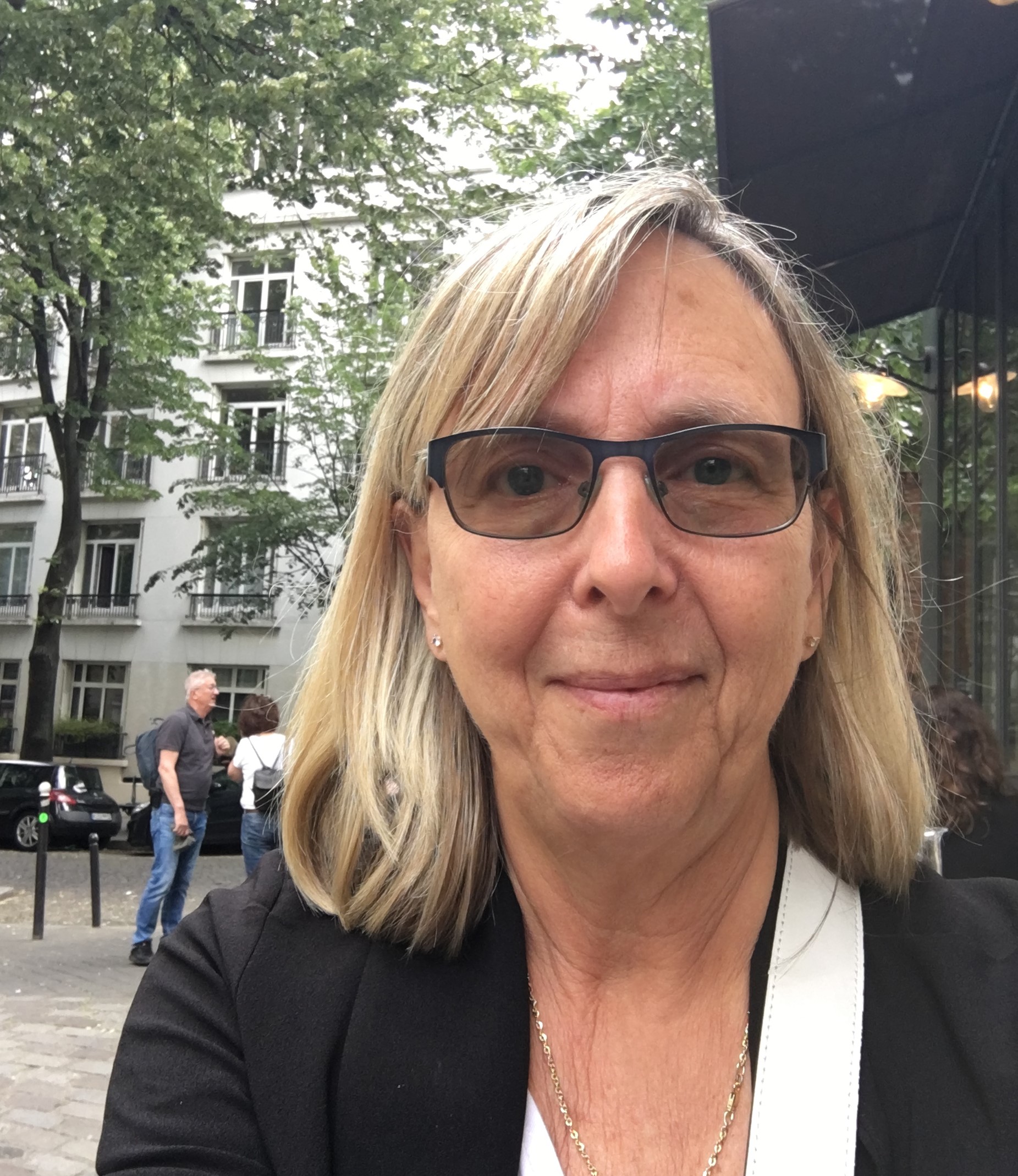 Portrait de Christiane Boulva, femme aux cheveux blonds portant des lunettes et un blazer noir, photographiée en milieu urbain